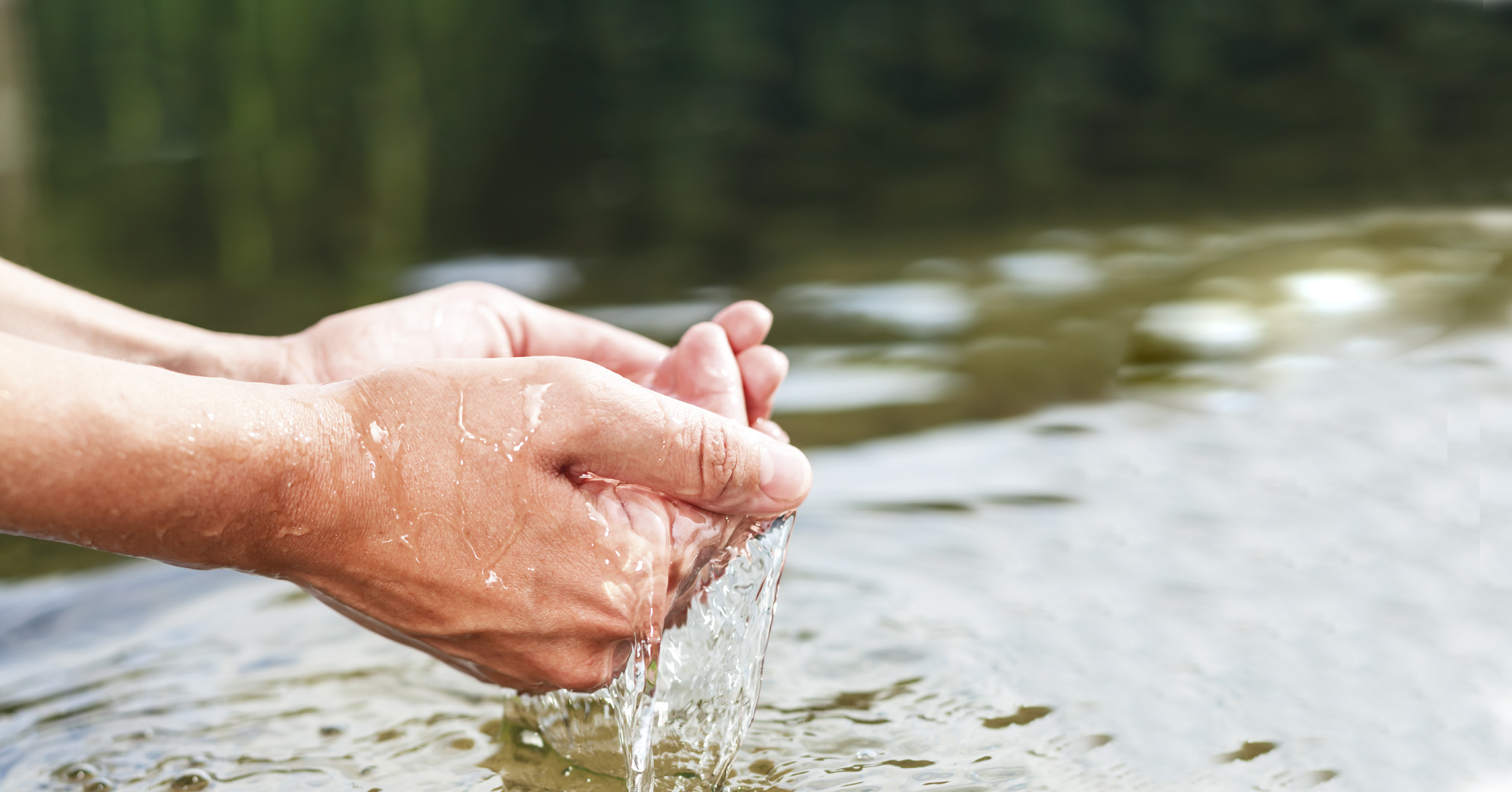 Duas mãos unidas em formato de concha pegam água em um rio